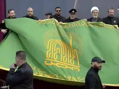 پرچم بارگاه مطهر امام رضا(ع) توسط خادمین رضوی به محل تشییع پیکر شهیدان نصرالله و صفی‌الدین رسید + فیلم